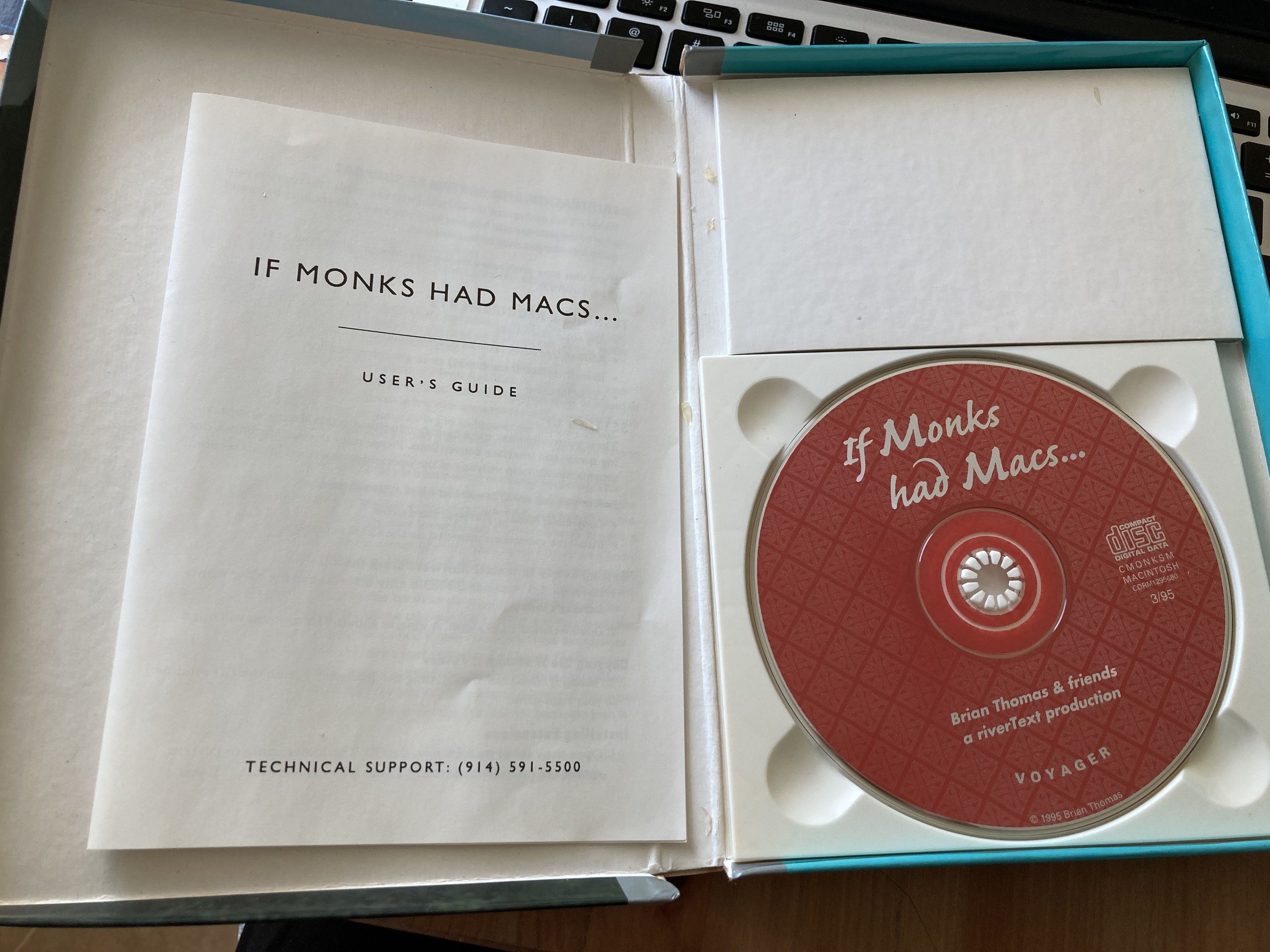The interior of If Monks Had Macs, showing a plain black and white manual, and a CD-ROM.
